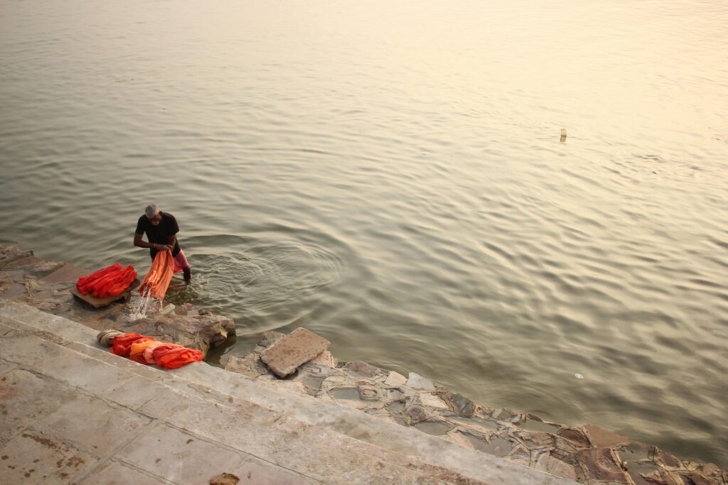 A man washing clothes by the river in Varanasi at sunset, showcasing traditional lifestyle.