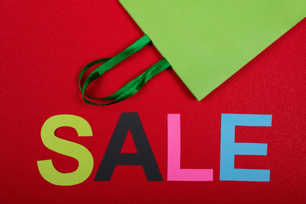 Vibrant sale text with green paper bag on a red background, perfect for promotions.